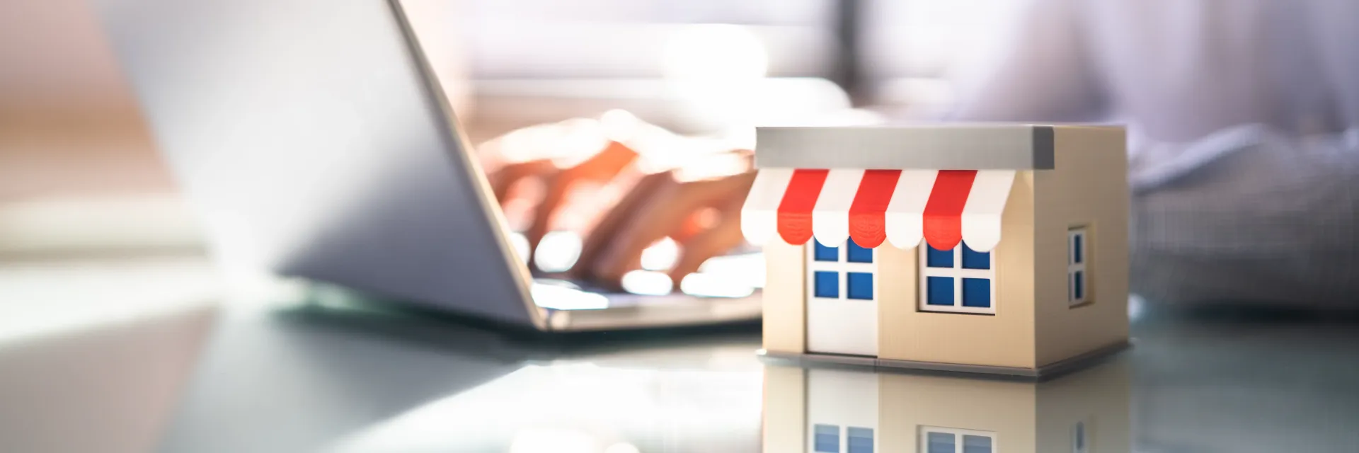 Someone typing on a laptop next to a scale model of a storefront.